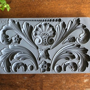 May include: A gray silicone mold with the text "IOD" in the top left corner. The mold features a variety of decorative floral and leaf designs.