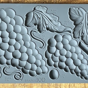 May include: A gray silicone mold with the text "GRAPES1OD" and various grape and leaf shapes. The mold is designed for making edible decorations, with measurements in milliliters and grams.