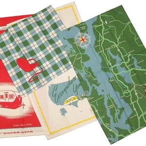 May include: Three vintage kitchen towels with a travel theme. One towel is red with a white camper and the text "Live Life on the Go" and "The SHIVER-STAR Deluxe Travel Trailer". Another towel is green and white plaid. The third towel is white with a map of the United States and the text "Everywhere You Go".