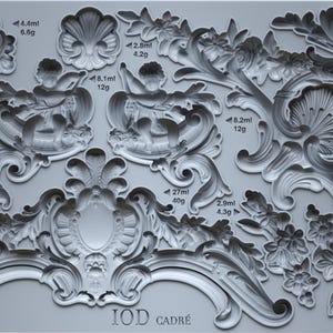 May include: A gray silicone mold featuring various ornate, baroque-style decorative elements. Designs include floral patterns, cherubs, and scrollwork, with measurements in milliliters and grams. The text "IOD CADRÉ" is visible.
