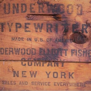 Peut inclure: Gros plan sur une caisse en bois avec les mots "UNDERWOOD TYPEWRITER" et "MADE IN U.S. OF AMERICA" imprim&eacute;s &agrave; l'encre fonc&eacute;e. La caisse comporte &eacute;galement le texte "UNDERWOOD ELMOTT FISHER COMPANY NEW YORK SALES AND SERVICE EVERYWHERE".