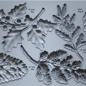 May include: A gray silicone mold featuring various winter foliage designs, including holly with berries, pine needles, and pine cones. The text "IOD WINTER FORAGE" is printed on the top left corner.