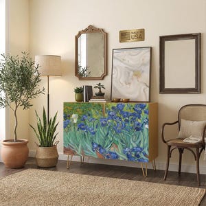 May include: A rectangular wooden cabinet with two doors featuring a printed reproduction of Vincent van Gogh's Irises painting. The cabinet stands on four thin gold-toned metal hairpin legs and has a smooth, light-colored wooden frame.