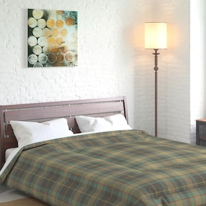 May include: A bedroom scene featuring a bed with a brown wooden headboard and a plaid comforter in shades of green, brown, and blue. White pillows and a white sheet are visible. A floor lamp with a beige lampshade stands beside the bed. A painting hangs on the white brick wall.