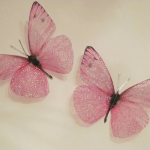 May include: Two pink glitter butterflies with translucent wings. The butterflies are on a white background.
