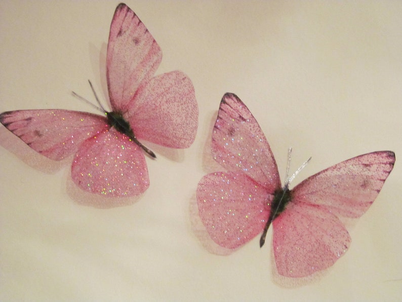 May include: Two pink glitter butterflies with translucent wings. The butterflies are on a white background.