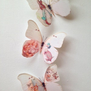 Könnte beinhalten: Drei weiße Schmetterlings-Wandaufkleber mit verschiedenen Illustrationen von Figuren aus Kinderbüchern. Die Schmetterlinge sind durchscheinend und haben einen zarten, Vintage-Look.