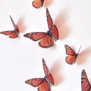 May include: A set of six orange and black monarch butterfly wall decals. The butterflies are arranged in a staggered pattern on a white background.