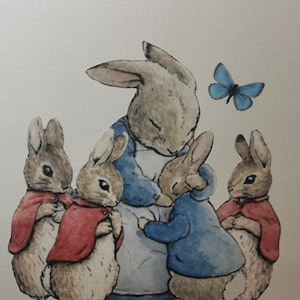Op de afbeelding: Een aquarel illustratie van een moederkonijn omringd door haar vier kinderen. De konijnen zijn in bruin- en grijstinten, de moeder draagt een blauwe jurk. De kinderen dragen rode en blauwe capes. Een blauwe vlinder is op de achtergrond.