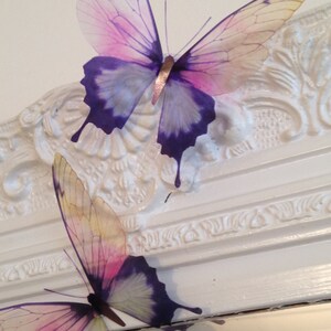 May include: Two decorative butterflies with purple and pink wings. The butterflies are made of a translucent material and have a delicate, feminine look.