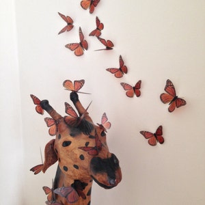 May include: A wooden giraffe sculpture with a brown and black spotted pattern.  The giraffe's head is turned to the side and its mouth is slightly open.  The giraffe is decorated with numerous orange and brown butterfly cutouts.