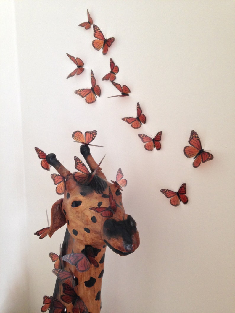 May include: A wooden giraffe sculpture with a brown and black spotted pattern.  The giraffe's head is turned to the side and its mouth is slightly open.  The giraffe is decorated with numerous orange and brown butterfly cutouts.