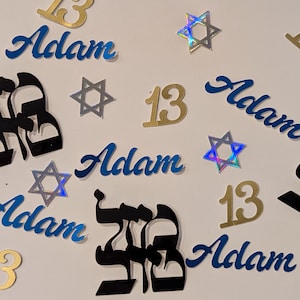 Peut inclure: Éléments décoratifs pour une célébration de Bar Mitzvah, avec le nom "Adam" en bleu, des lettres hébraïques, des découpes dorées du chiffre 13 et des formes d'étoiles de David. Certaines étoiles sont holographiques.