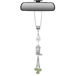 May include: Silver car charm featuring a rearview mirror attachment. The charm has a decorative design with a cowboy boot, a swirl, and green beaded accents. The charm hangs from a silver chain.