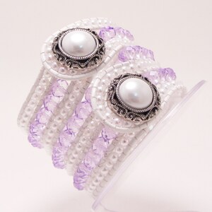May include: A white beaded bracelet with two silver and pearl accents. The bracelet is wrapped in multiple rows of white beads and lavender beads.