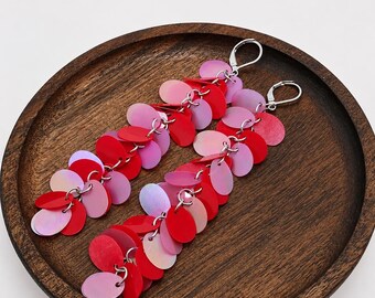 May include: A pair of long dangle earrings featuring multiple overlapping oval-shaped sequins in shades of red, pink, and iridescent white. The sequins are attached to silver-toned metal jump rings and secured with silver-toned lever-back closures.