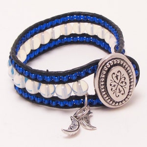 May include: A black leather bracelet with blue beads and white opal stones. The bracelet has a silver clasp with a decorative design and two silver crescent moon charms.