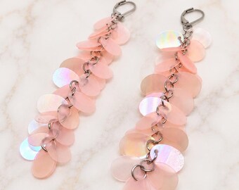May include: A pair of long dangle earrings featuring multiple pale pink, iridescent, circular sequins attached to silver-toned metal jump rings. The earrings have a lever-back closure and a cascading, layered design that creates a shimmering effect.