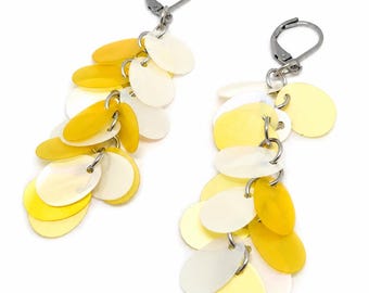 May include: A pair of dangle earrings featuring multiple oval-shaped discs in shades of yellow and off-white. The discs are attached to silver-toned metal lever-back closures, creating a layered, cascading effect that hangs from the top hook.