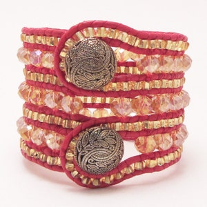 May include: A red leather wrap bracelet with gold accents and clear crystals. The bracelet has two decorative metal buttons.