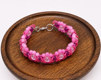 May include: A beaded bracelet featuring a repeating pattern of vibrant pink, magenta, and clear faceted crystal beads. The circular design is constructed with small seed beads and includes a silver-toned metal lobster claw clasp closure.