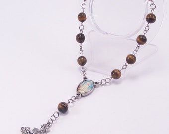 May include: A rosary with brown tiger eye beads and a silver-toned metal chain. The rosary features a crucifix and an oval centerpiece with a religious image. The beads are approximately 0.3 inches in diameter.