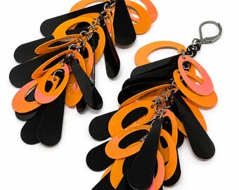 May include: A pair of dangle earrings featuring a cluster of layered, glossy black and bright orange teardrop-shaped and oval-shaped plastic charms. The charms are suspended from dark metal lever-back hooks by small silver-toned metal jump rings.