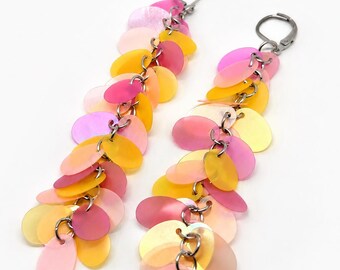 May include: A pair of long dangle earrings featuring multiple overlapping oval-shaped sequins in shades of pink, yellow, and peach. The sequins are attached to silver-toned metal jump rings and secured with silver-toned lever-back earring closures.