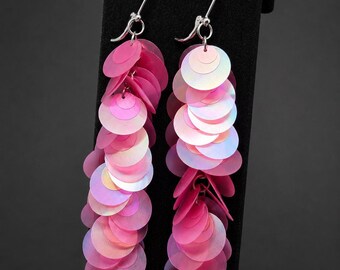 May include: A pair of long dangle earrings featuring multiple circular, iridescent pink sequins layered to create a cascading effect. The earrings are attached to silver-toned metal fishhook wires, providing a secure and lightweight design.