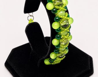 May include: A beaded bracelet featuring a dense cluster of round beads in various shades of lime green, emerald green, and translucent yellow-green. The design incorporates small seed beads and larger smooth spherical beads arranged in a textured pattern.