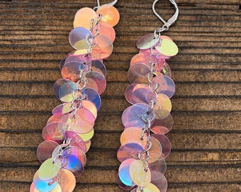 May include: A pair of long dangle earrings featuring multiple iridescent, circular sequins in shades of pink, orange, and blue. The sequins are linked together with silver-toned metal rings and attached to silver-toned lever-back earring hooks.