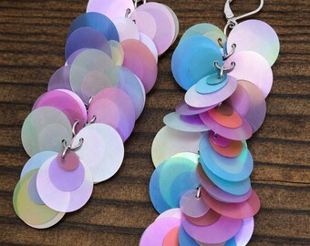May include: A pair of dangle earrings featuring multiple iridescent, circular sequins in shades of pink, blue, purple, and green. Each earring is attached to a silver-toned metal lever-back closure, creating a layered, cascading effect of reflective, translucent, and opaque round discs.