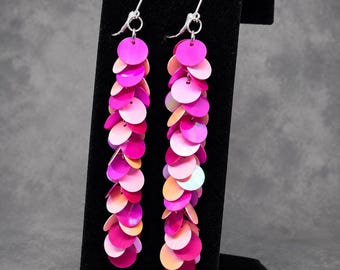 May include: A pair of long dangle earrings featuring multiple circular sequins in shades of hot pink, light pink, and orange. The sequins are layered and attached to silver-toned metal ear wires with a secure lever-back closure mechanism.