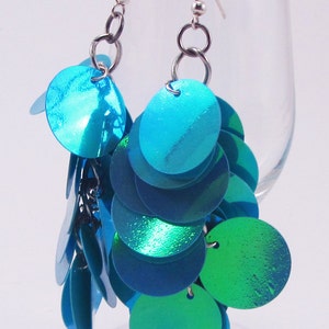 May include: A pair of dangle earrings with silver hooks and multiple turquoise and green iridescent round sequins.