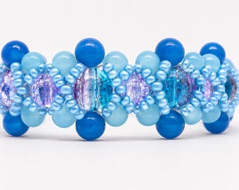 May include: A beaded bracelet featuring a repeating pattern of large, round, dark blue and light blue beads interspersed with smaller, light blue seed beads and translucent, crackled, purple and teal glass beads arranged in a woven design.