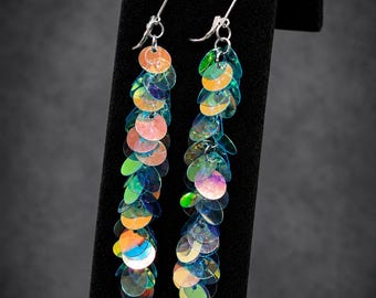May include: A pair of long dangle earrings featuring multiple iridescent, circular sequins in shades of blue, green, and orange. The sequins are layered to create a cascading effect, attached to silver-toned metal ear wires with a lever-back closure.