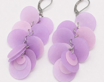 May include: A pair of dangle earrings featuring multiple overlapping circular discs in varying shades of light and medium purple. The discs are suspended from silver-toned metal lever-back closures, creating a layered, cascading design.