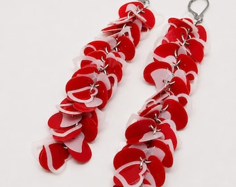 May include: A pair of long dangle earrings featuring a cascading arrangement of numerous small, flat, heart-shaped discs in vibrant red and translucent white. The hearts are linked together with silver-toned metal rings and attached to silver-toned lever-back closures.
