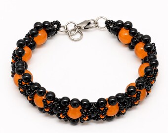 May include: A beaded bracelet featuring a repeating pattern of round, glossy black beads and vibrant orange beads. The bracelet is constructed with a woven design and includes a silver-toned metal lobster claw clasp and jump rings for closure.