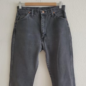 May include: A pair of dark gray denim jeans with a straight leg fit. The jeans have a button fly and belt loops.