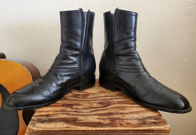 May include: A pair of black leather boots with a zipper up the back of each boot. The boots have a pointed toe and a low heel.