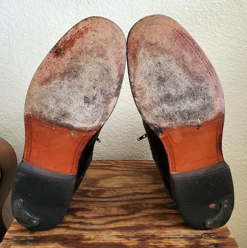 May include: A pair of black leather dress shoes with brown leather soles. The shoes are worn and have a distressed look.