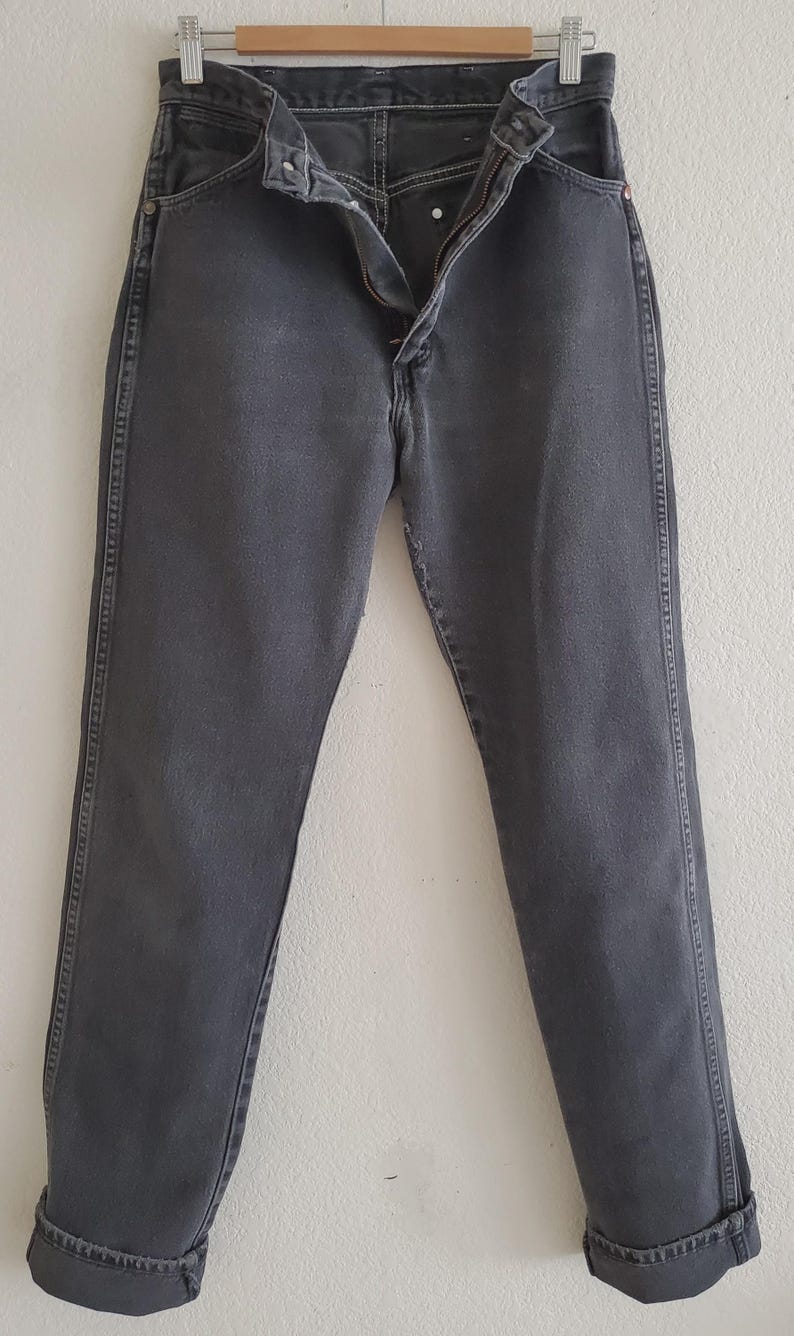 May include: A pair of dark gray denim jeans with a button fly and a straight leg.