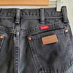 May include: Black denim jeans with a brown leather patch that says "Wrangler" on the back pocket.
