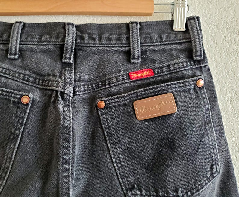 May include: Black denim jeans with a brown leather patch that says "Wrangler" on the back pocket.