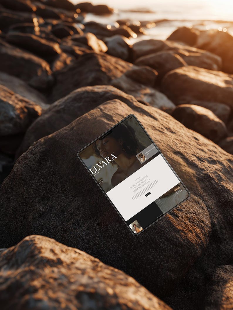 May include: A tablet displaying a website with the text "ELVARA" on the screen. The tablet is resting on a large, dark rock, with other rocks and the ocean in the background. The website features images and text.