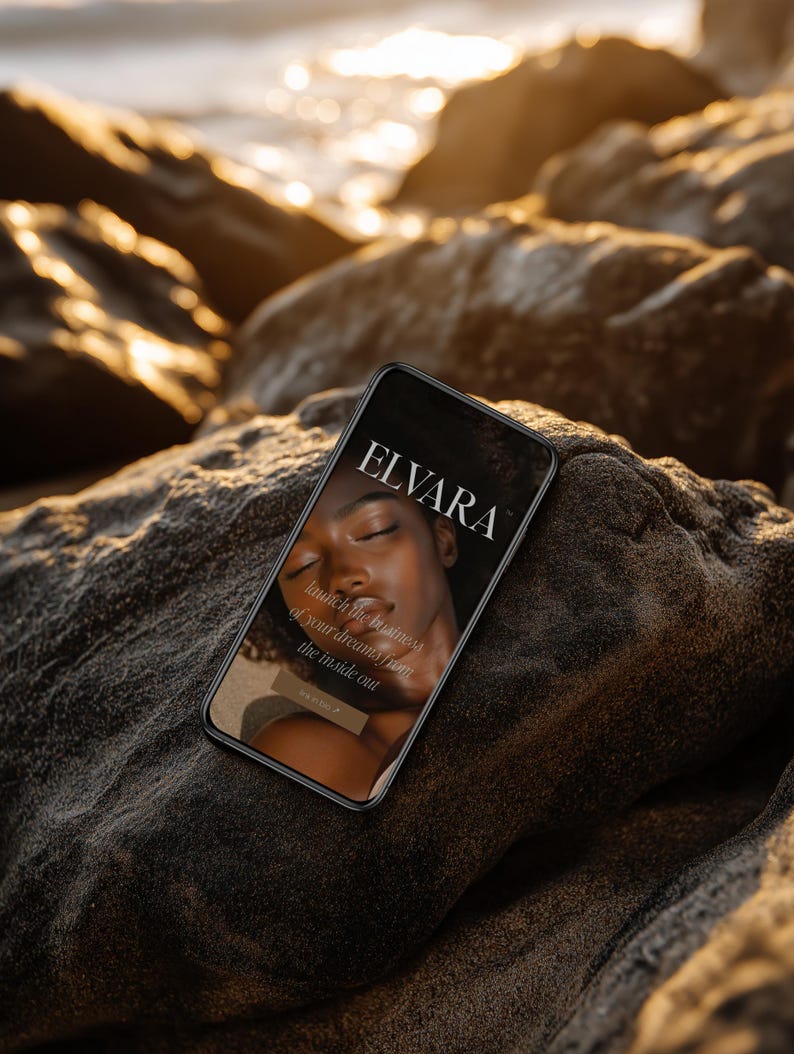 May include: A smartphone displaying the "ELVARA" logo and text "launch the business of your dreams from the inside out." The phone is resting on a dark, textured rock formation, with a blurred ocean and sunlight in the background.