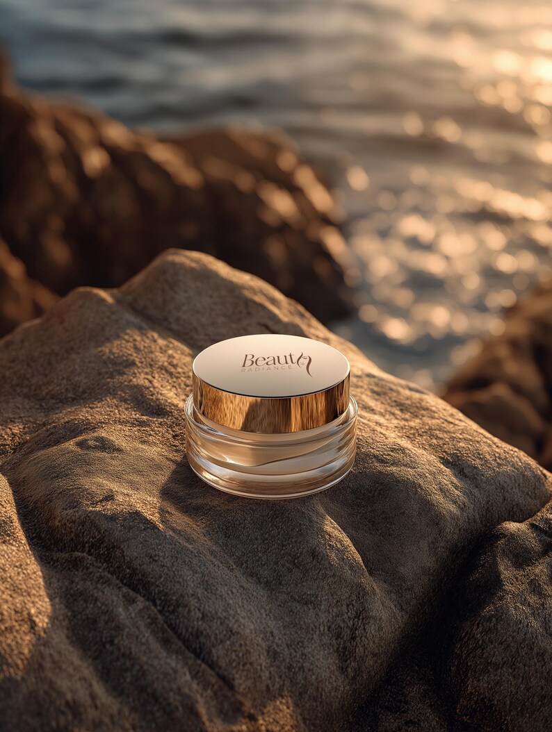 May include: A clear glass jar with a gold lid, labeled "Beauty Radiance", sits on a textured rock. The jar contains a cream-colored substance. The background shows a blurred view of the ocean and rocks, with sunlight reflecting on the water.