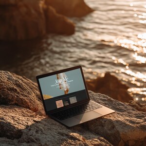 May include: A black laptop computer with the screen displaying the words "Join Me" and "This is more than a business." The laptop is open and resting on a large, textured rock near the ocean. The scene is bathed in warm sunlight.