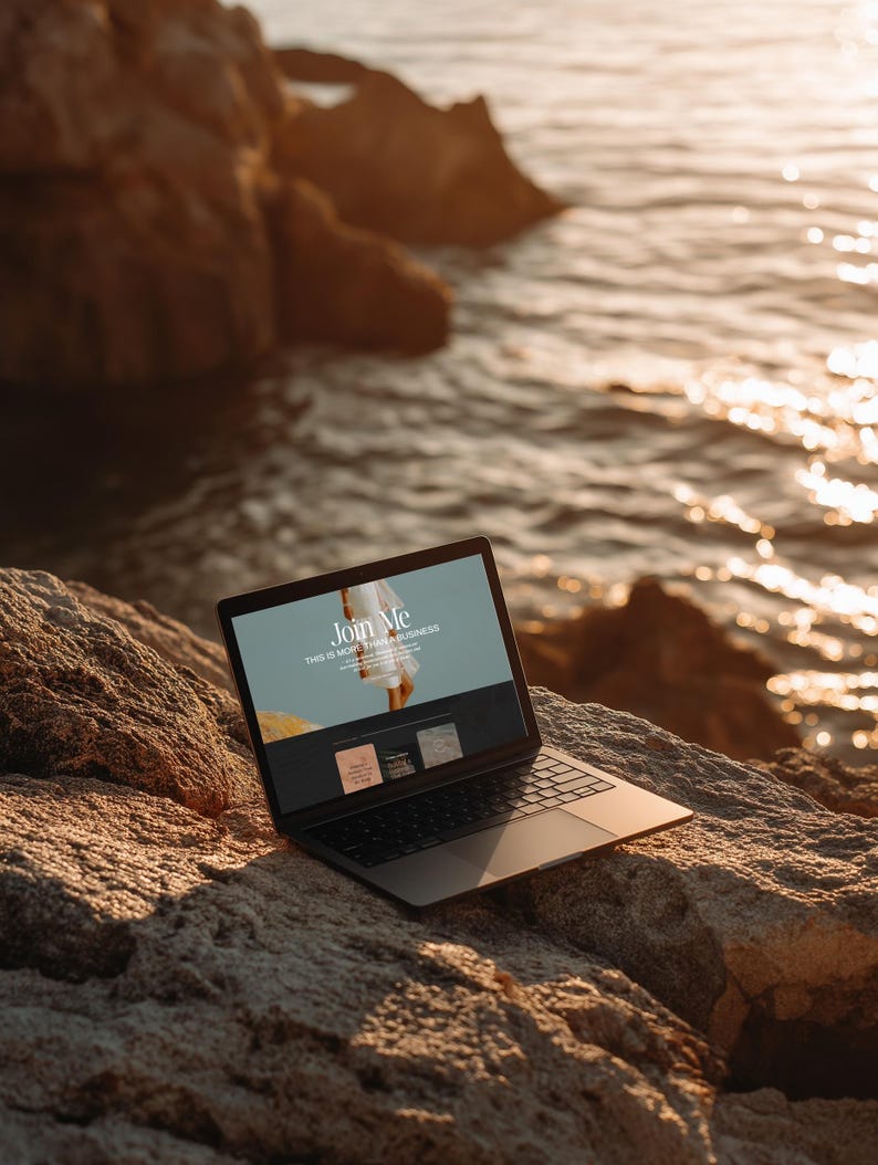 May include: A black laptop computer with the screen displaying the words "Join Me" and "This is more than a business." The laptop is open and resting on a large, textured rock near the ocean. The scene is bathed in warm sunlight.